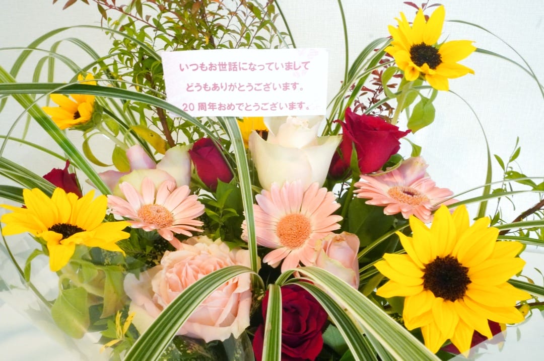 ひまわりやバラなどの花束と日本語のカードです。
